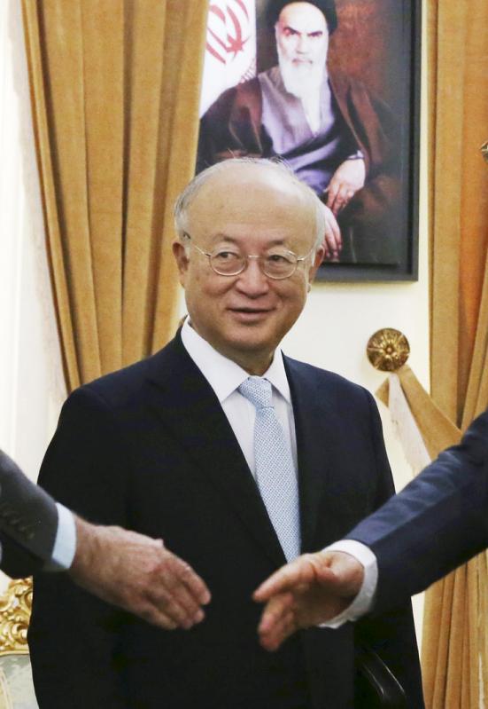 FILE - In this July 2, 2015 file photo, U.N. nuclear chief Yukiya Amano stands as Secretary of Iran's Supreme National Security Council Ali Shamkhani shakes hands with delegation members before the start of their meeting in Tehran, Iran. Iran's state TV is reporting Amano has arrived in Tehran, to 