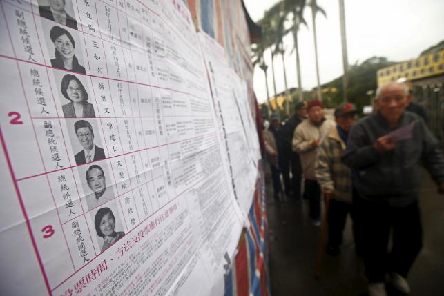 Voters queue next to a poster of candidates to cast their ballots at a polling station during general elections in New Taipei City, Taiwan January 16, 2016.  REUTERS/Pichi Chuang