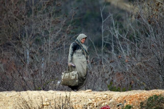 An internally displaced Syrian woman, covered with mud, carries her belongings as she is stuck with others in the town of Khirbet Al-Joz, in Latakia countryside, waiting to get permission to cross into Turkey near the Syrian-Turkish border, Syria, February 7, 2016. REUTERS/Ammar Abdullah