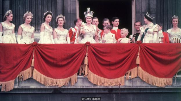 2nd June 1953:  The newly crowned Queen Elizabeth II waves to the crowd from the balcony at Buckingham Palace. Her children Prince Charles and Princess Anne stand with her.  (Photo by Hulton Archive/Getty Images)